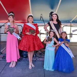Pageant winners holding trophies on stage.