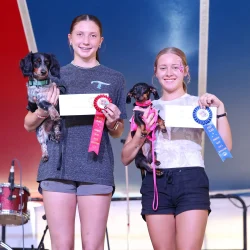 Two girls with dogs and prize ribbons.