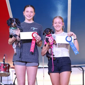 Two girls with dogs and prize ribbons.